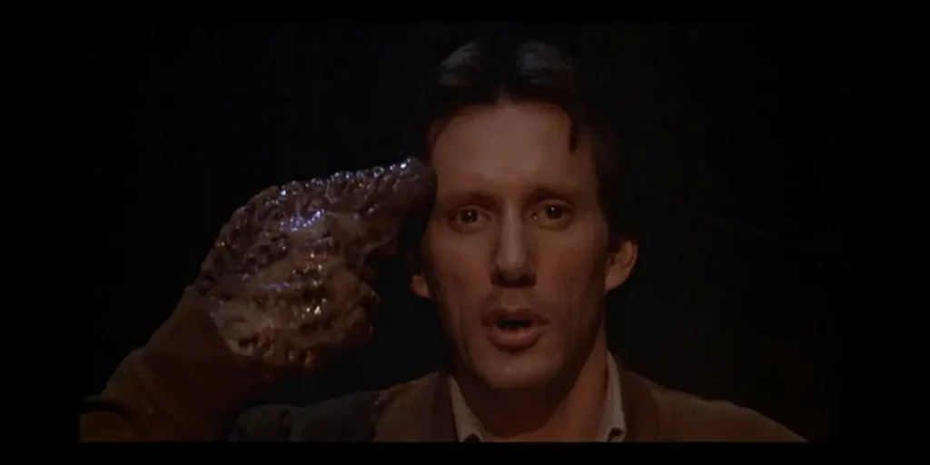 Fotograma de un hombre con una pistola orgánica apuntando a su cabeza, escena icónica del body horror en el cine.