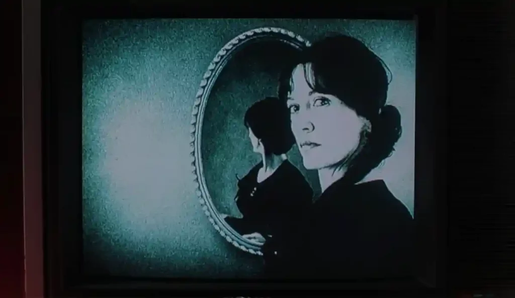 Imagen en blanco y negro de una mujer reflejada dos veces en un espejo ovalado, con una mirada fija y desconcertante.