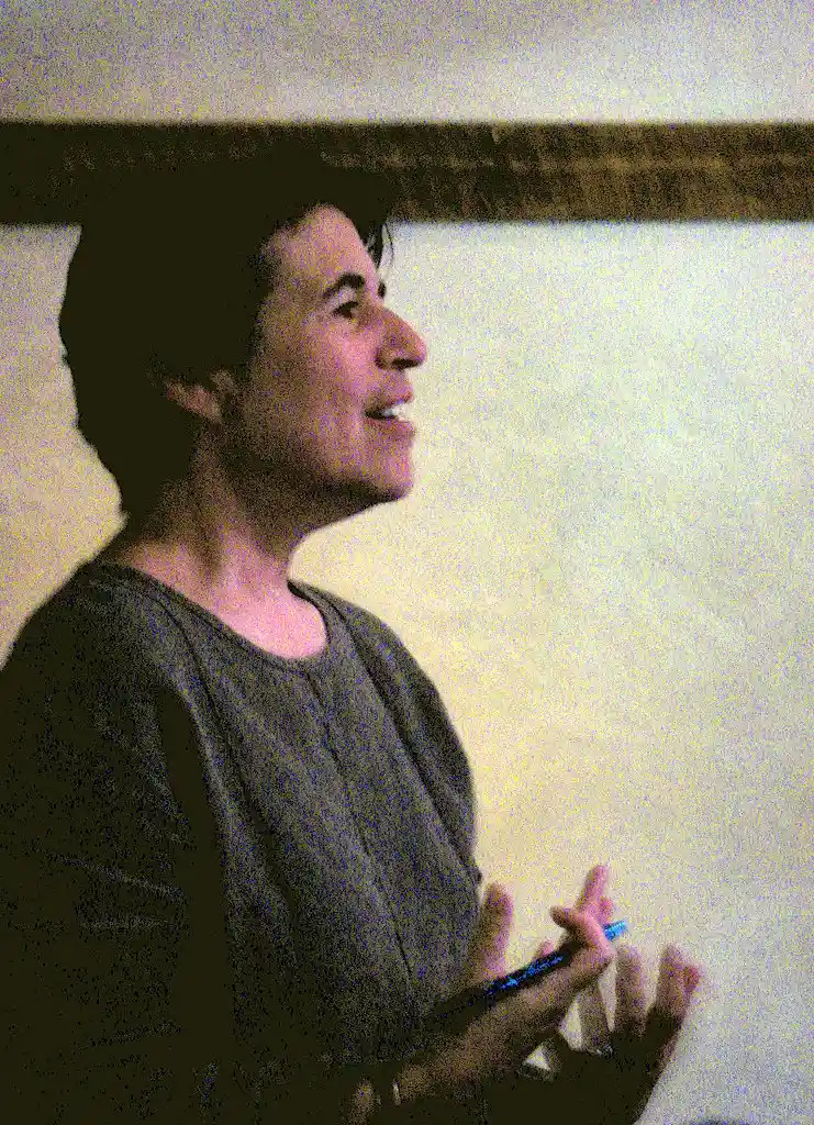 Escritora Natalie Goldberg de perfil, sonriendo mientras sostiene un bolígrafo, durante una charla o taller.