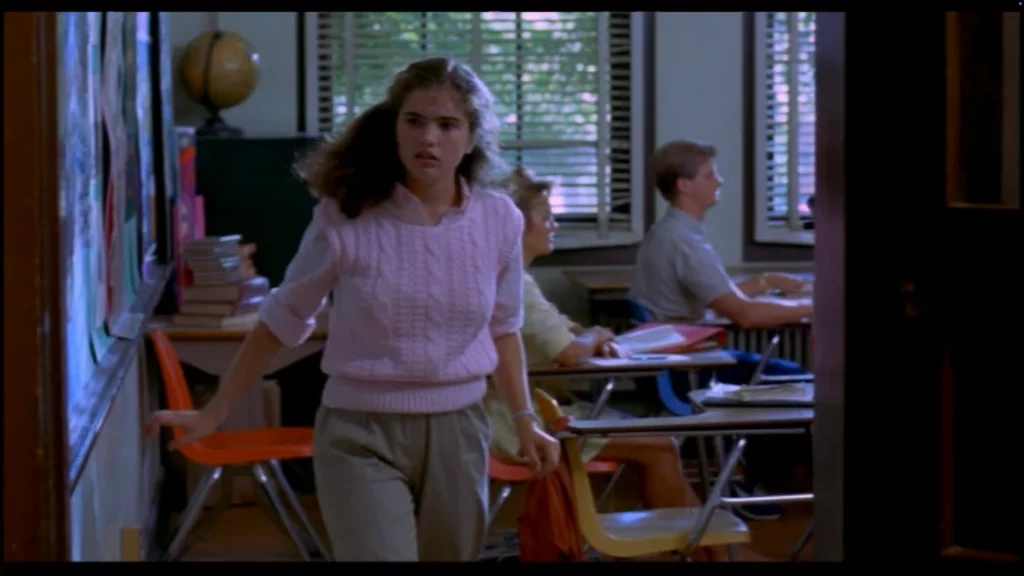 Adolescente cruza la puerta de un aula luminosa; pupitres y estudiantes al fondo, atmósfera de inquietud.
