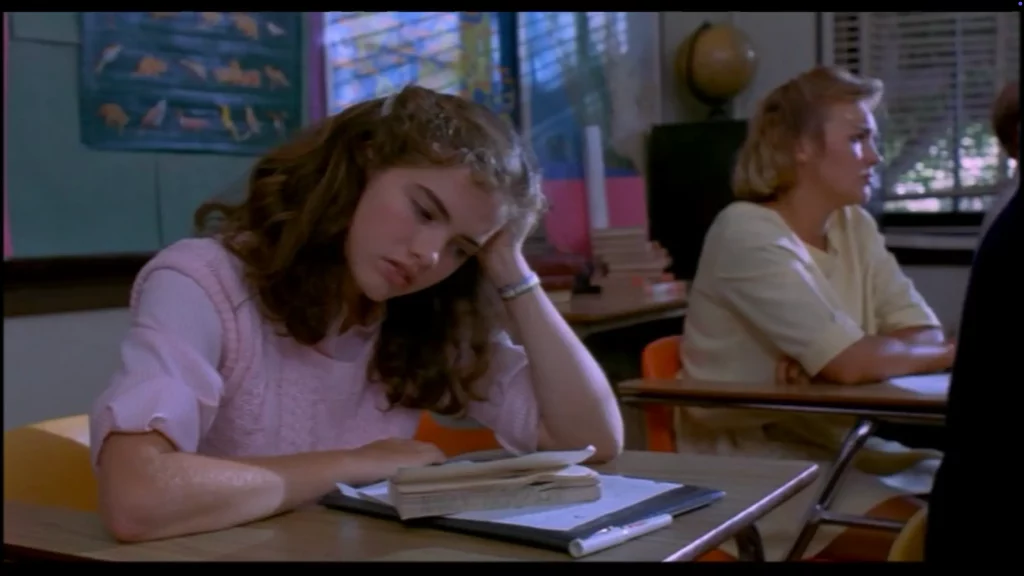 Nancy somnolienta en su pupitre durante una clase, con la cabeza apoyada en la mano y un libro abierto delante.