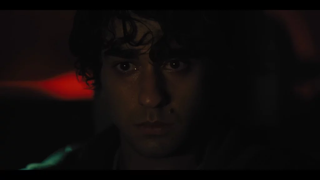 Primer plano oscuro de Peter dentro del coche, mirada fija al frente con leve luz roja al fondo.