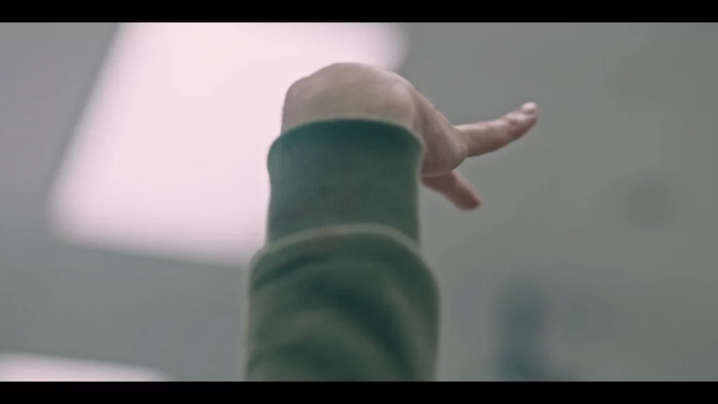 Mano de un estudiante que se alza rígida en un aula, gesto involuntario bajo luz fría de fluorescente.